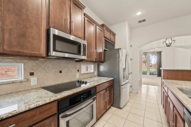 kitchen featuring arched walkways, stainless steel appliances, visible vents, decorative backsplash, and light stone countertops