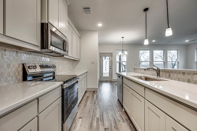 kitchen with sink, hanging light fixtures, white cabinets, and appliances with stainless steel finishes