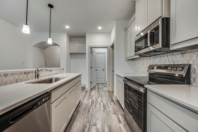 kitchen featuring appliances with stainless steel finishes, decorative light fixtures, sink, backsplash, and light wood-type flooring