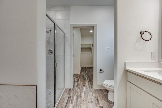 bathroom with vanity, wood finished floors, a stall shower, a spacious closet, and toilet
