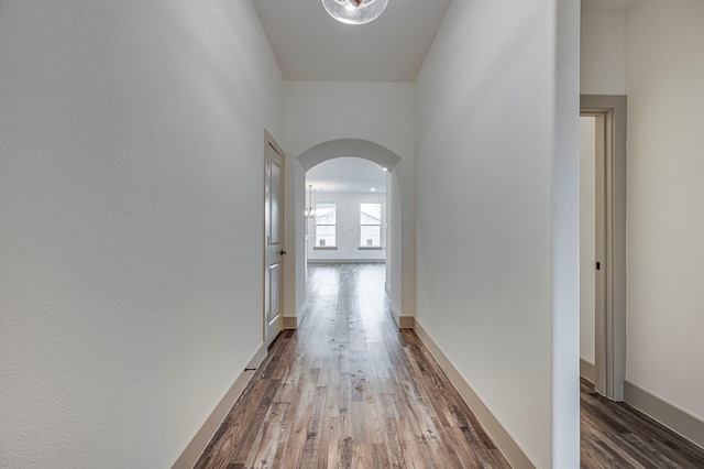 corridor with wood finished floors, arched walkways, and baseboards