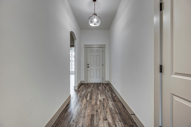 hall with arched walkways, baseboards, and dark wood-style flooring