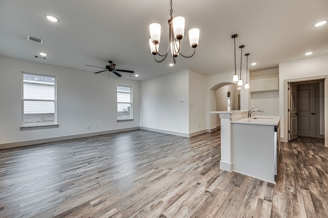 kitchen featuring hardwood / wood-style floors, ceiling fan with notable chandelier, decorative light fixtures, white cabinets, and a center island with sink