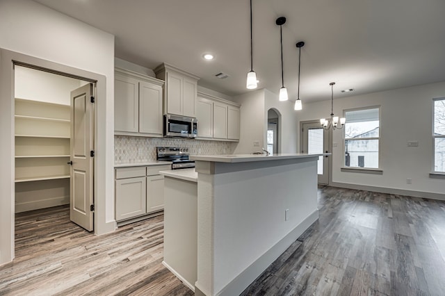 kitchen with tasteful backsplash, decorative light fixtures, a center island with sink, light hardwood / wood-style flooring, and stainless steel appliances