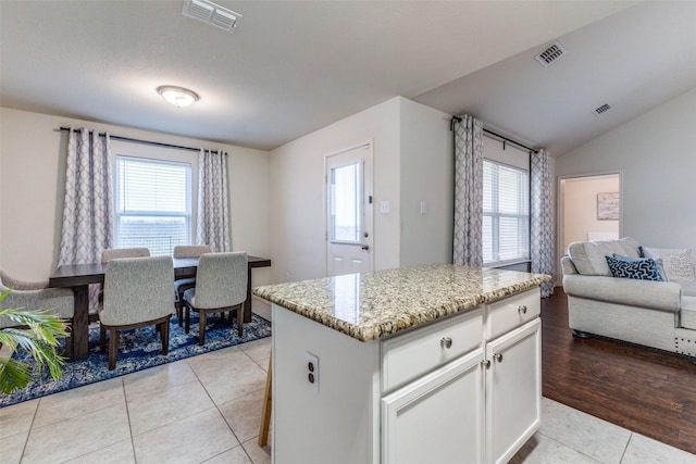 kitchen featuring light tile patterned flooring, a kitchen island, white cabinetry, lofted ceiling, and light stone counters