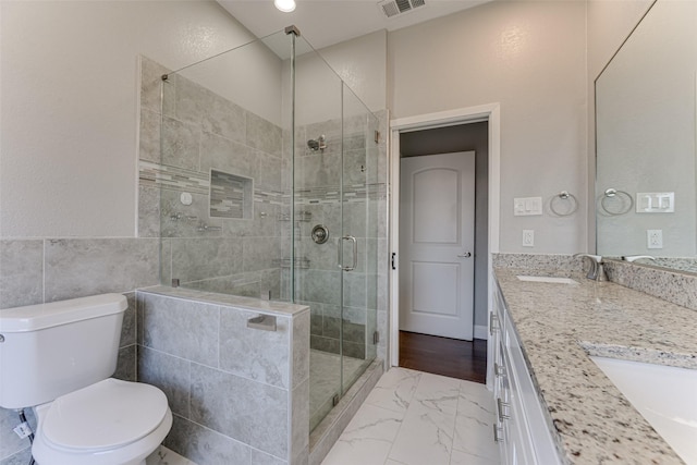 bathroom featuring a shower stall, double vanity, marble finish floor, toilet, and a sink