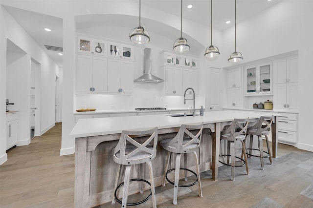 kitchen featuring pendant lighting, sink, white cabinets, a large island with sink, and wall chimney exhaust hood