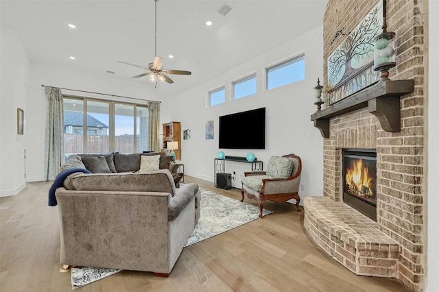 living room featuring a brick fireplace, light hardwood / wood-style floors, and ceiling fan