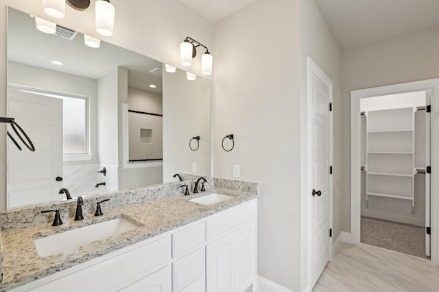 bathroom featuring a sink, baseboards, double vanity, and a spacious closet