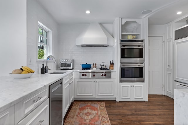 kitchen with sink, appliances with stainless steel finishes, light stone countertops, white cabinets, and custom exhaust hood