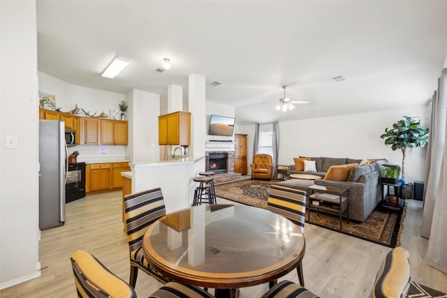 dining room featuring ceiling fan, a brick fireplace, sink, and light hardwood / wood-style floors