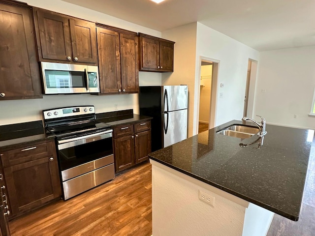 kitchen featuring sink, dark stone countertops, dark hardwood / wood-style flooring, a kitchen island with sink, and stainless steel appliances