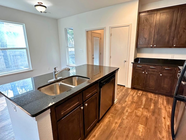 kitchen with sink, dishwasher, dark stone countertops, hardwood / wood-style floors, and an island with sink