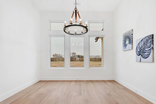 unfurnished dining area with an inviting chandelier and light wood-type flooring