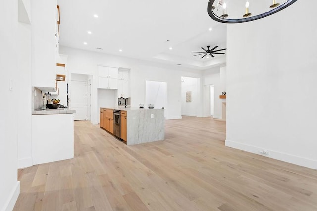 kitchen with ceiling fan with notable chandelier, sink, white cabinets, a raised ceiling, and light hardwood / wood-style flooring