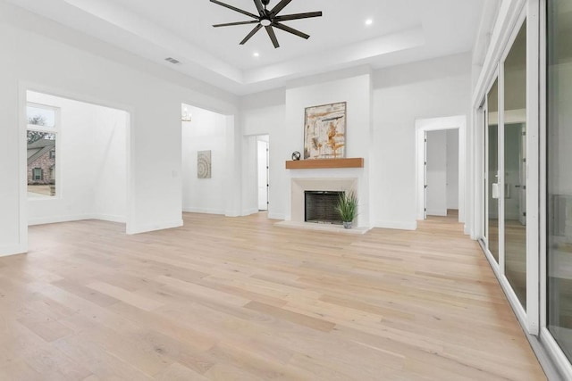 unfurnished living room featuring ceiling fan, a tray ceiling, light hardwood / wood-style floors, and a high ceiling