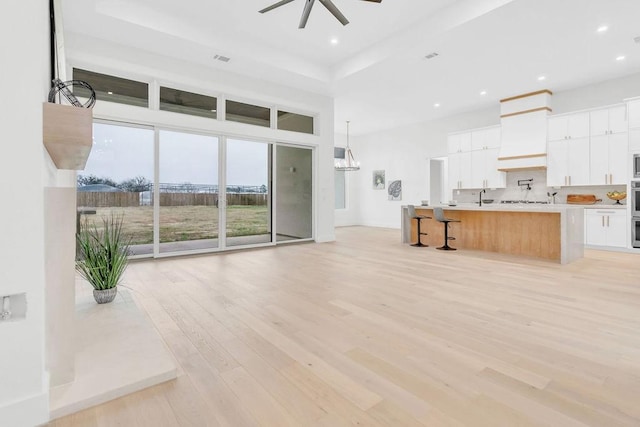 kitchen with sink, custom exhaust hood, light hardwood / wood-style flooring, a raised ceiling, and ceiling fan with notable chandelier