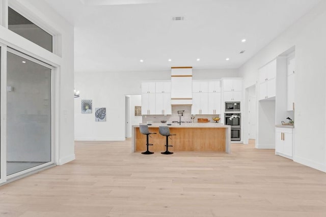 kitchen with built in microwave, a breakfast bar, an island with sink, and white cabinets