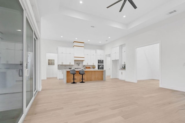 kitchen featuring custom exhaust hood, a center island with sink, white cabinets, and light wood-type flooring