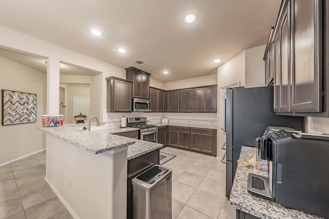 kitchen featuring light tile patterned floors, appliances with stainless steel finishes, light stone counters, dark brown cabinetry, and kitchen peninsula