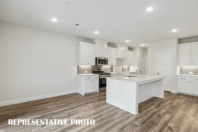 kitchen featuring tasteful backsplash, white cabinetry, stainless steel appliances, a center island with sink, and light wood-type flooring