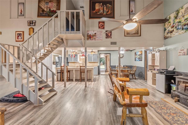 living area featuring light wood finished floors, a towering ceiling, visible vents, a ceiling fan, and stairway