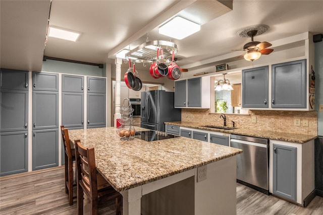 kitchen with stainless steel appliances, backsplash, a sink, gray cabinetry, and light wood-style flooring