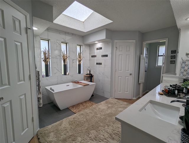 bathroom featuring a skylight, tile walls, a textured ceiling, vanity, and a washtub