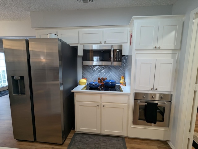 kitchen with appliances with stainless steel finishes, white cabinetry, wood-type flooring, backsplash, and a textured ceiling