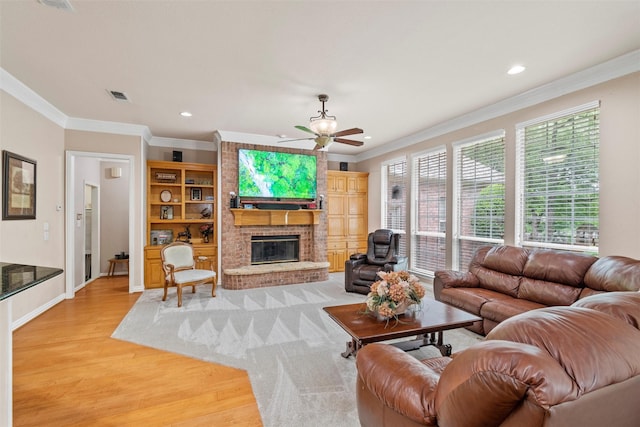 living room with crown molding, a brick fireplace, ceiling fan, and light wood-type flooring