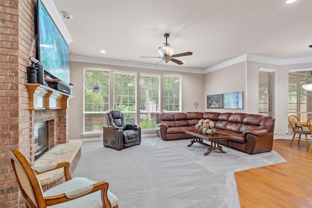 living room featuring ceiling fan, ornamental molding, a brick fireplace, and light wood-type flooring