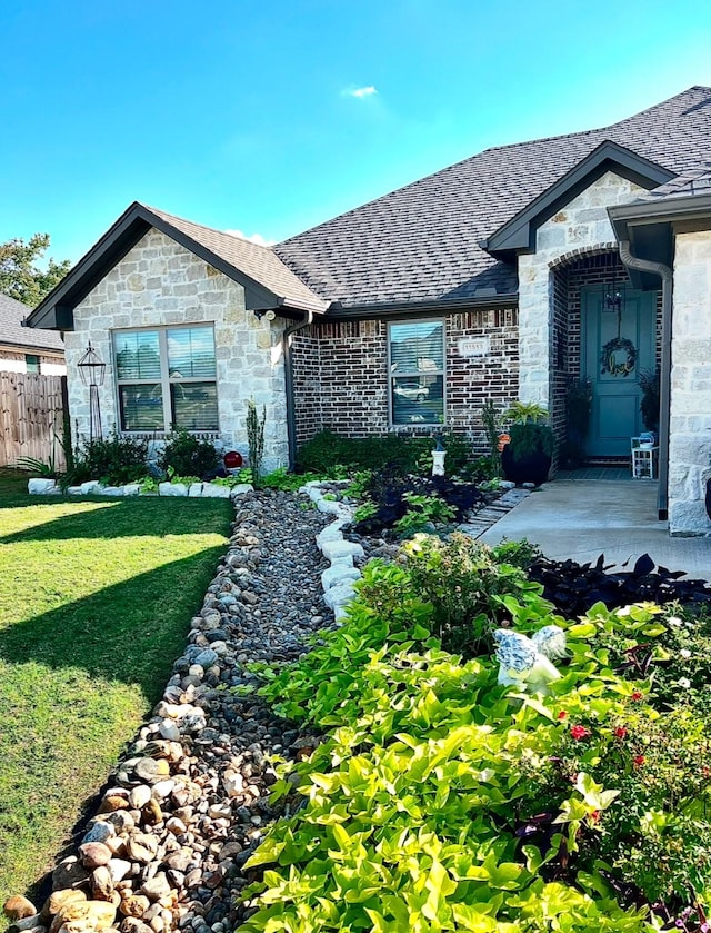 view of front facade with a front yard, stone siding, roof with shingles, and fence