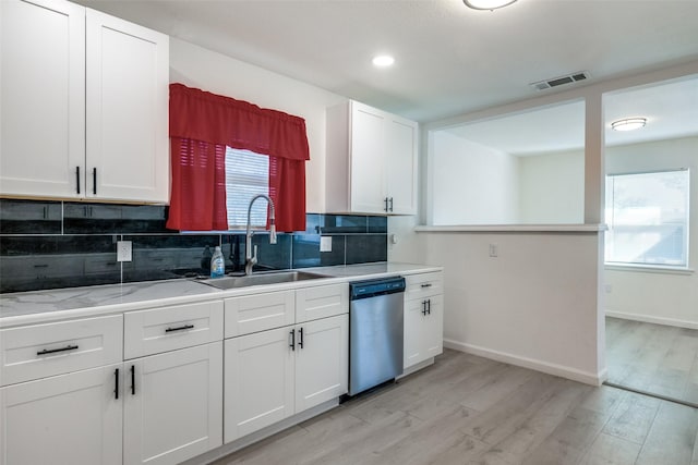 kitchen with sink, dishwasher, white cabinetry, light hardwood / wood-style floors, and decorative backsplash