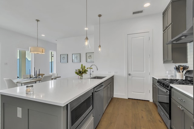 2125 Bird St, Fort Worth, TX 76111 - kitchen featuring stainless steel appliances, wall chimney range hood, gray cabinets, a peninsula, and wood finished floors
