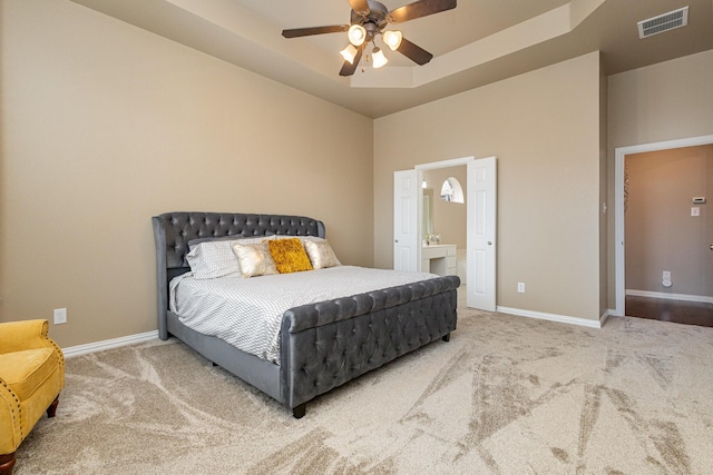 carpeted bedroom featuring connected bathroom, a raised ceiling, and ceiling fan