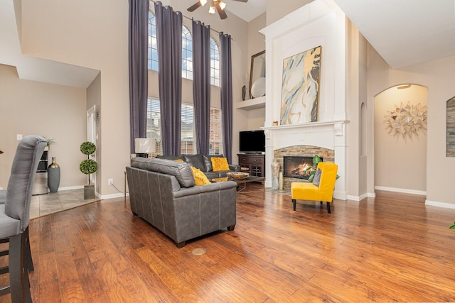 living room with ceiling fan, a towering ceiling, wood-type flooring, and a fireplace