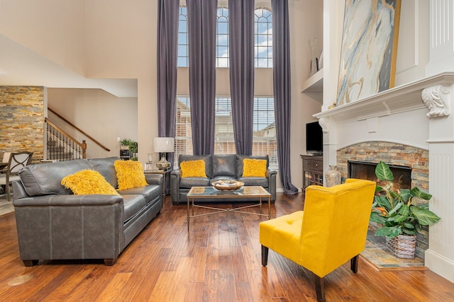 living room featuring hardwood / wood-style floors, a stone fireplace, and a high ceiling