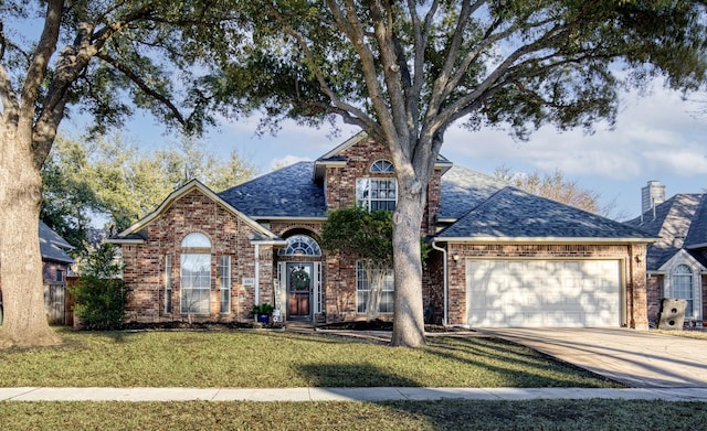 traditional-style home with an attached garage, brick siding, concrete driveway, roof with shingles, and a front yard