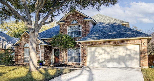 traditional-style house featuring brick siding, a shingled roof, concrete driveway, an attached garage, and a front lawn