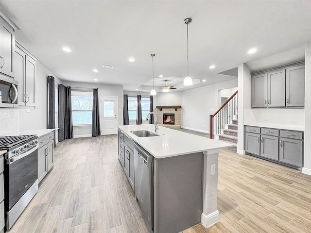 kitchen with gray cabinets, sink, hanging light fixtures, a kitchen island with sink, and stainless steel appliances