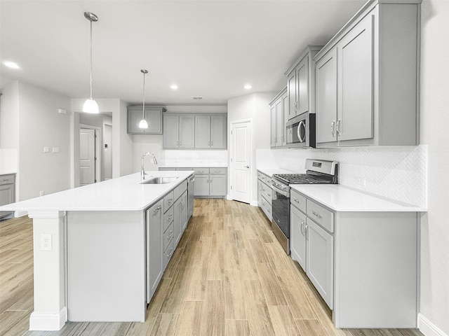 kitchen featuring gray cabinets, appliances with stainless steel finishes, an island with sink, sink, and hanging light fixtures