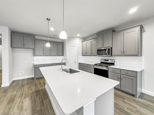 kitchen with an island with sink, appliances with stainless steel finishes, gray cabinets, and sink