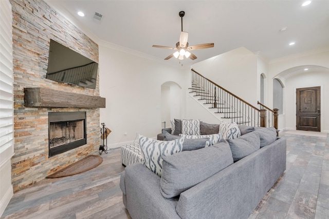 living room with ceiling fan, ornamental molding, a stone fireplace, and wood-type flooring