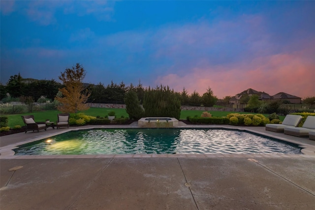 pool at dusk featuring a patio area, an outdoor pool, fence, and an in ground hot tub