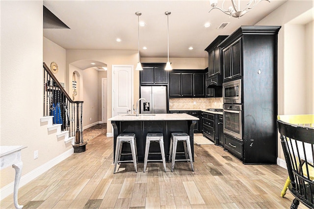 kitchen with appliances with stainless steel finishes, a breakfast bar area, decorative backsplash, hanging light fixtures, and a center island with sink