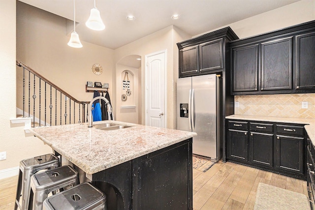 kitchen with sink, a breakfast bar area, decorative light fixtures, a center island with sink, and stainless steel fridge