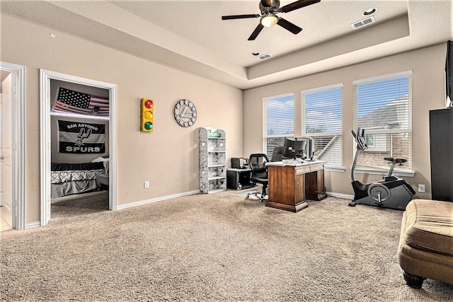 carpeted office with ceiling fan and a tray ceiling