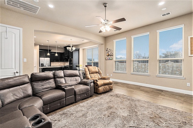 living room with ceiling fan with notable chandelier and hardwood / wood-style floors