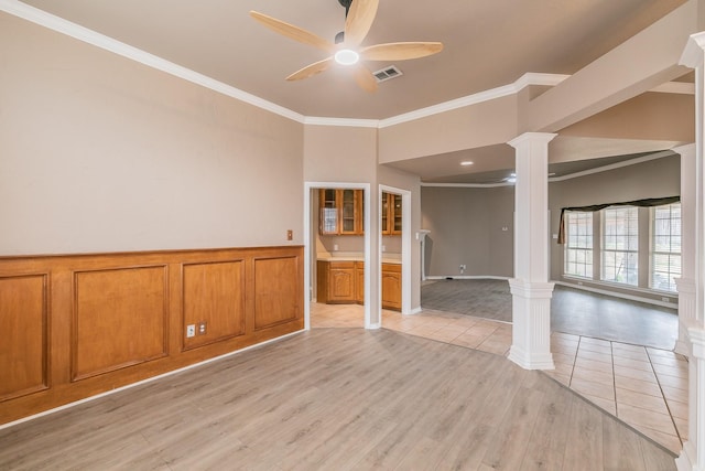 spare room featuring decorative columns, ornamental molding, a ceiling fan, wainscoting, and light wood-type flooring