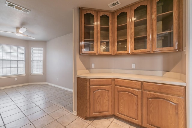 kitchen featuring visible vents, light countertops, brown cabinetry, and glass insert cabinets